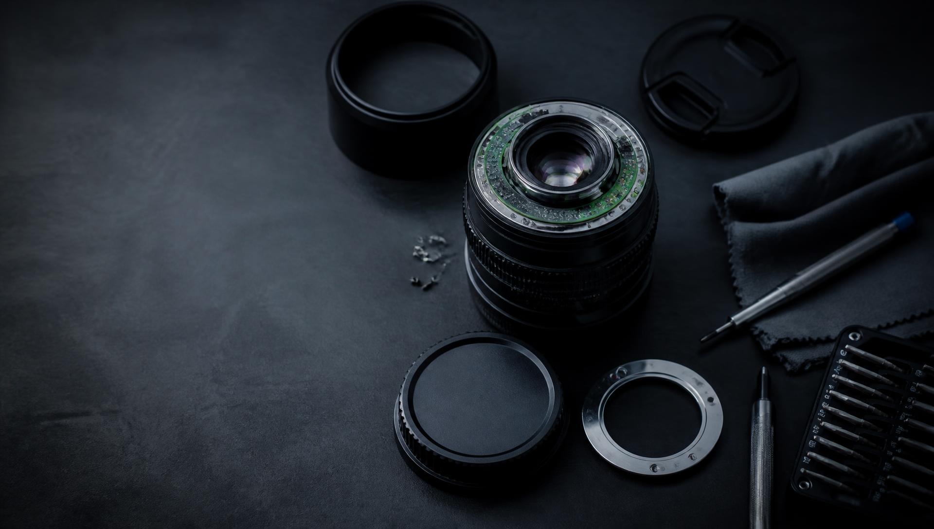 Camera lens being serviced on a technician's workbench with precision tools